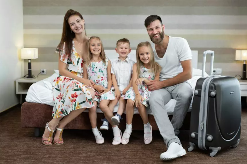 Parents with children sit on the bed in the hotel and laugh. Traveling with children